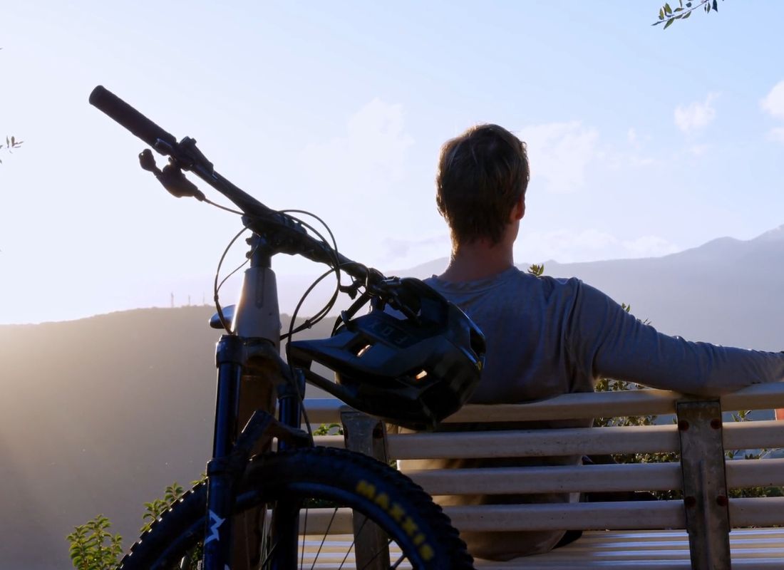 momak sedi na klupici, iza njega električni bicikl